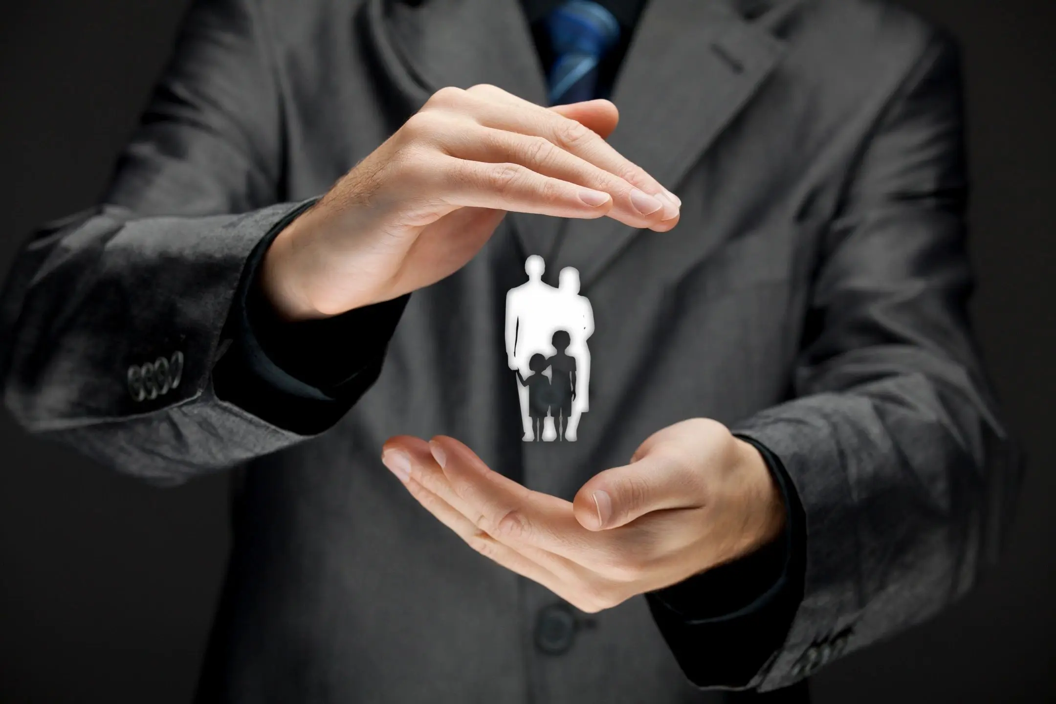 Businessman protecting a paper cutout family between his hands.