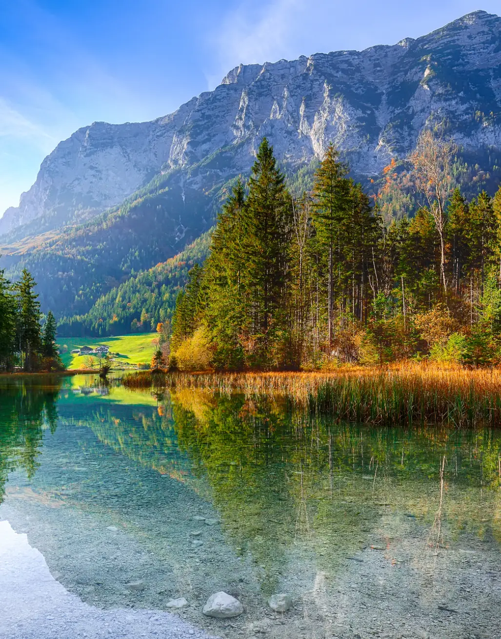 Serene lake reflecting trees and mountains under a clear sky.